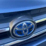 A close-up view of a blue Toyota cars front grille, featuring a silver bumper, white Toyota logo, and visible headlights and license plate.