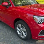 A red 2021 Subaru Forester parked on a gravel driveway, surrounded by a lush green lawn and trees in the background.